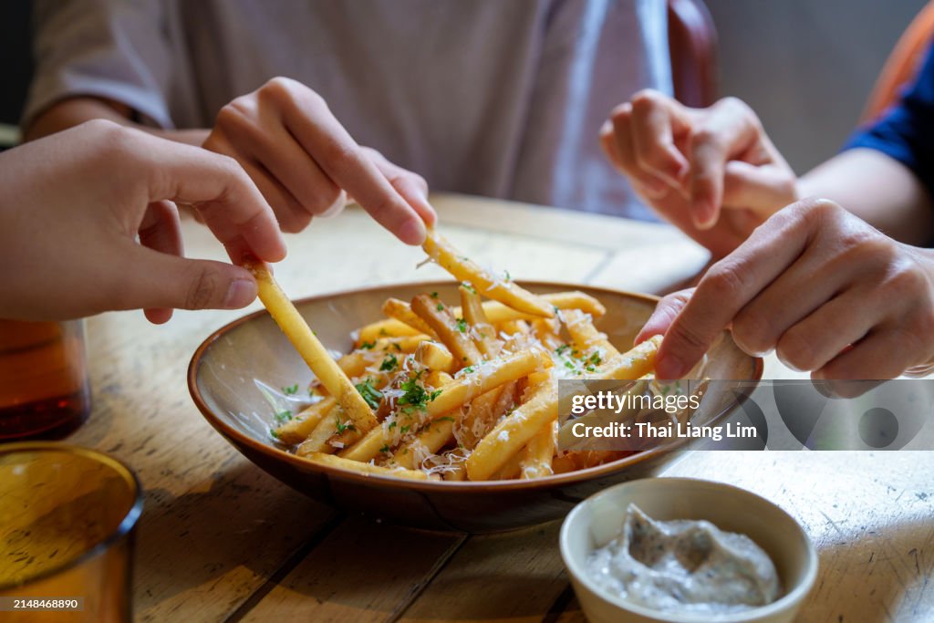Friends sharing and enjoying fries topped with Parmesan cheese and truffled mayonnaise sauce.