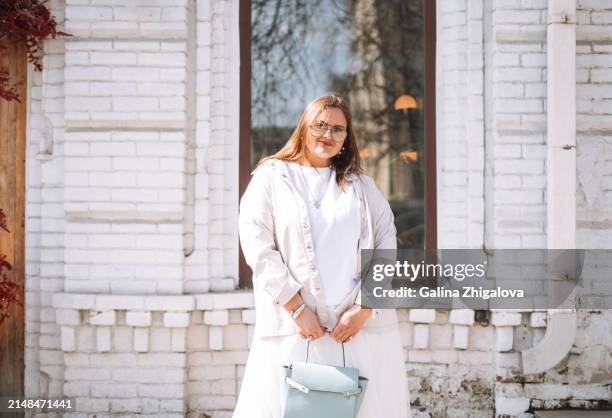 fashionable smiling young woman plus size in white clothes on city street - plus size stock pictures, royalty-free photos & images