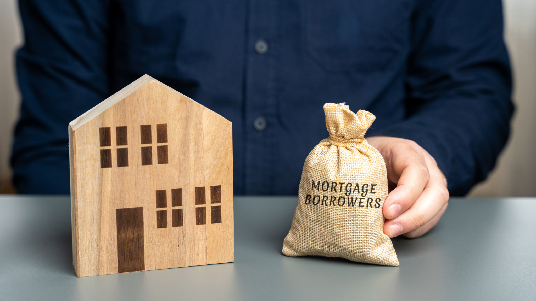 Mortgage borrowers concept. Individuals or entities who have taken out a mortgage loan from a lender to finance the purchase of a property. Money bag and miniature house Mortgage borrowers concept. Individuals or entities who have taken out a mortgage loan from a lender to finance the purchase of a property. Money bag and miniature house
