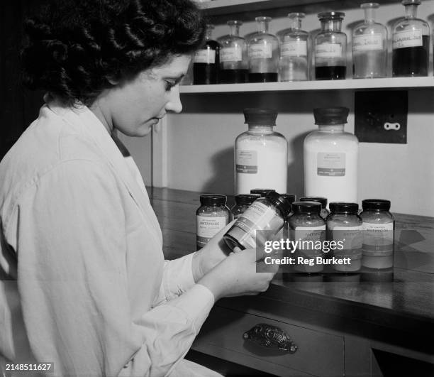 Lab technician inspects a bottle of Antrycide, with more bottles on the counter before her, and more jars on the shelves in the background, the...