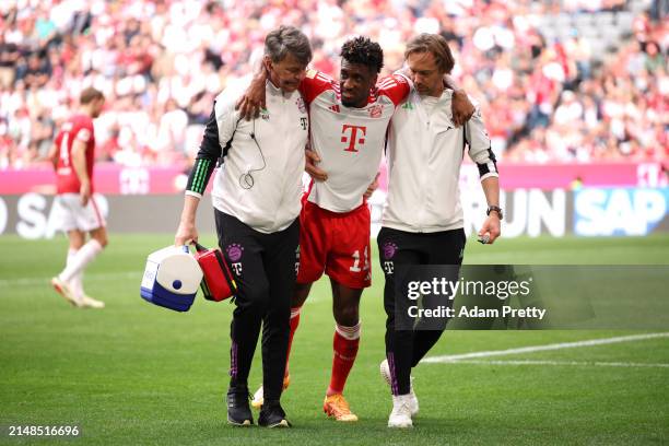 Kingsley Coman of Bayern Munich leaves the pitch with the help of medical staff following an injury during the Bundesliga match between FC Bayern...