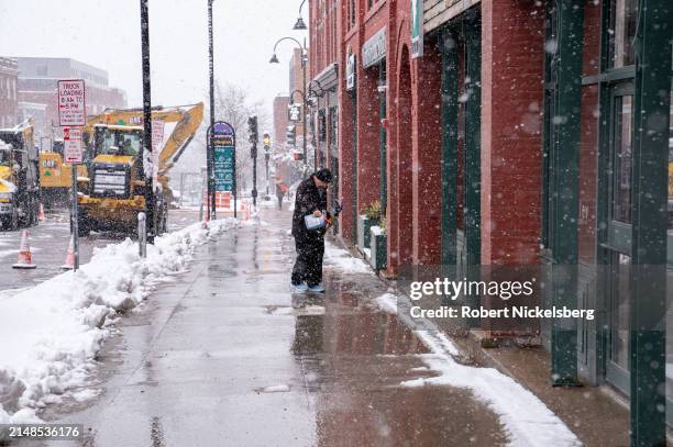 Man sprinkles salt while clearing a sidewalk during a late spring snowfall April 4, 2024 in Burlington, Vermont. Large areas of northern Vermont had...