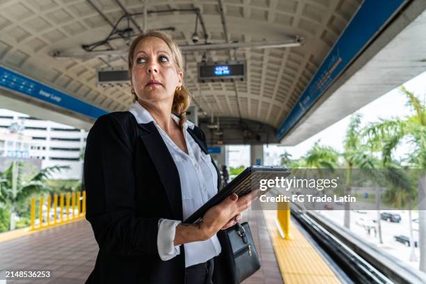 mature businesswoman using digital tablet and waiting the train on station - elevated train stock pictures, royalty-free photos & images