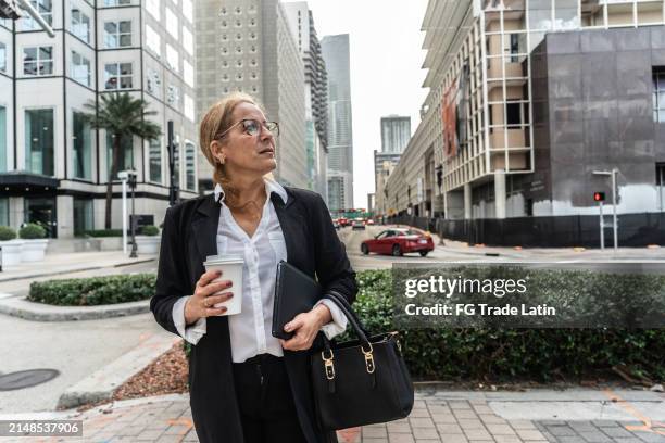 mujer madura mirando a su alrededor y caminando por la ciudad - mirar alrededor fotografías e imágenes de stock