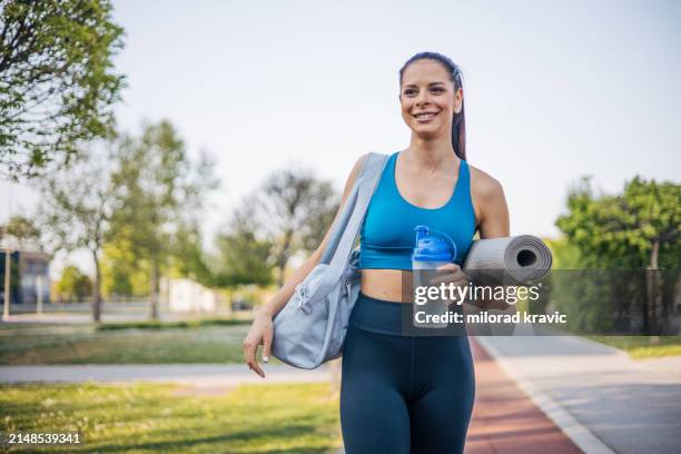 young sporty woman walking with sport bag and exercise mat in hand - mat stock pictures, royalty-free photos & images