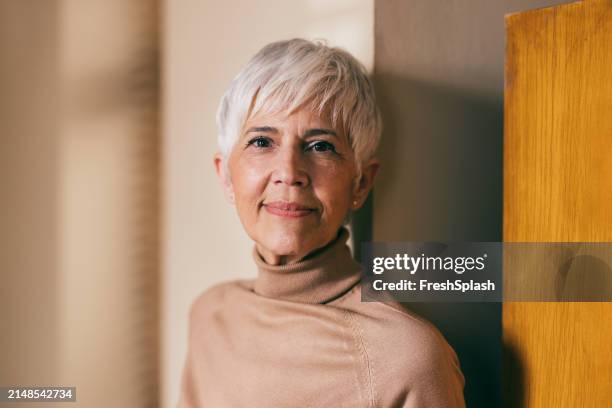 senior woman in turtleneck standing by wooden door - warm light stock pictures, royalty-free photos & images