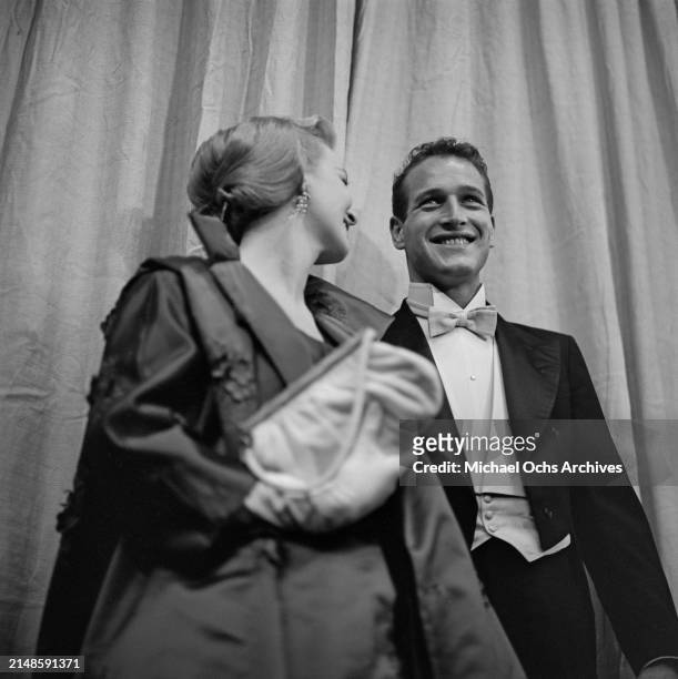 American actress Joanne Woodward, wearing a coat with white evening gloves, and a purse in her left hand, and her husband, American actor Paul...