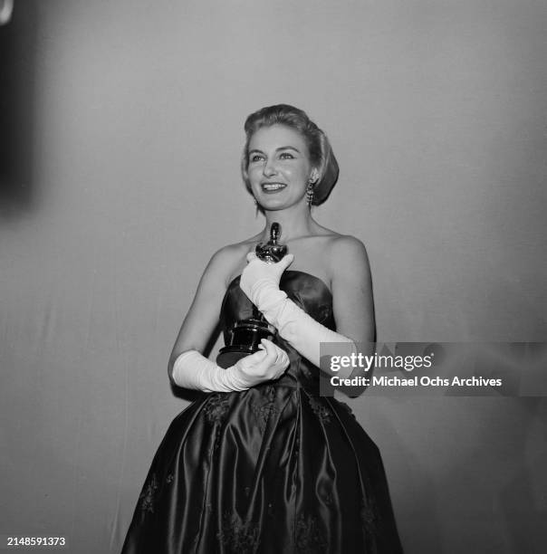 American actress Joanne Woodward, wearing a strapless evening gown with white evening gloves, in the 30th Academy Awards press room, at the RKO...