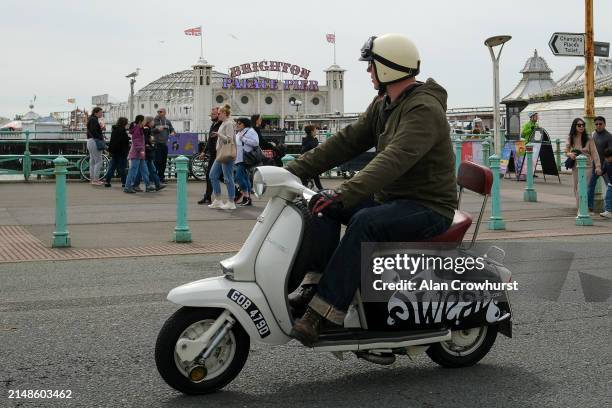 Rider and scooter pass the Brighton Palace Pier on the seafront on April 14, 2024 in Brighton, England. In May 1964, more than 1000 members of rival...