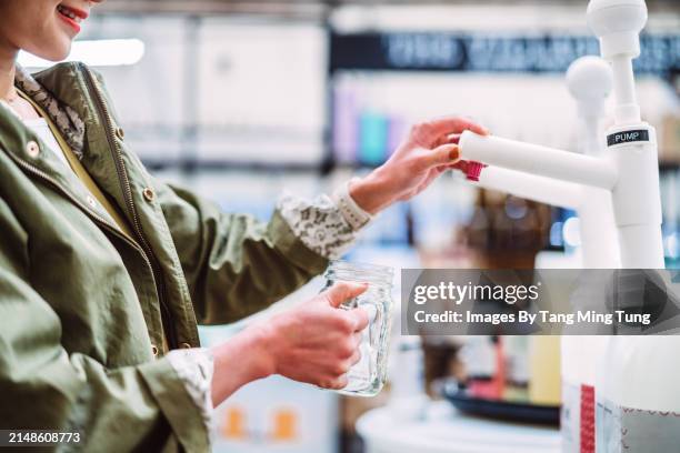 sustainable choices: a young asian woman refilling a glass jar with biodegradable cleaning product in zero-waste store - cleaning equipment stock pictures, royalty-free photos & images