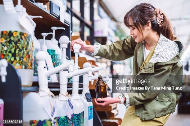 sustainable choices: a young asian woman refilling a reusable glass bottle with body care product in zero-waste store - ethical consumerism stock pictures, royalty-free photos & images
