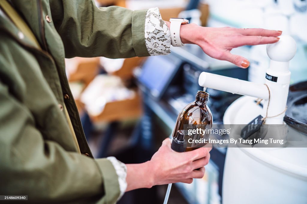 Sustainable Choices: A Young Female Shopper Refilling a Reusable Glass Bottle with Body Care Product in Zero-waste Store