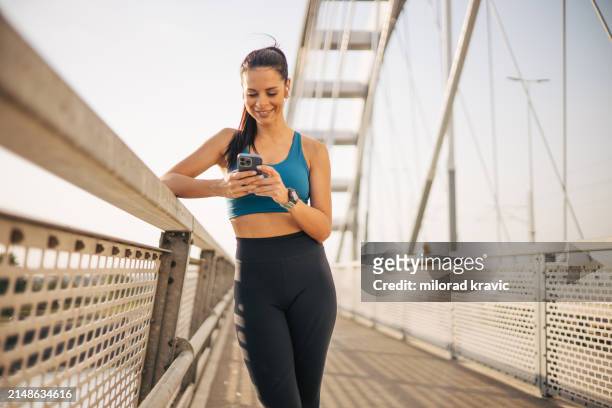 attractive sportswoman standing on a bridge and using a smartphone to write a message. - fitness or vitality or sport and women stockfoto's en -beelden