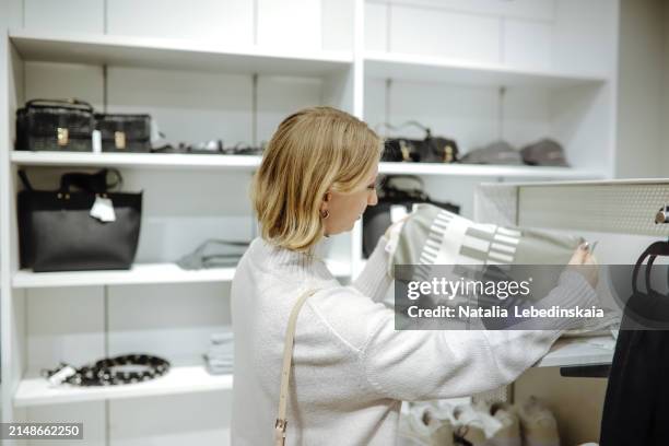 accessory choice: woman in a sweater picks out a scarf in a clothing store, focusing on accessorizing her outfit - accessorizing stockfoto's en -beelden