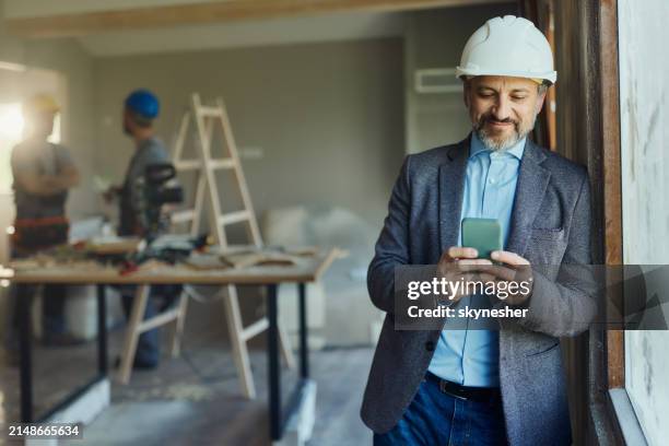 smiling male architect using mobile phone during home renovation. - real estate developer stock pictures, royalty-free photos & images