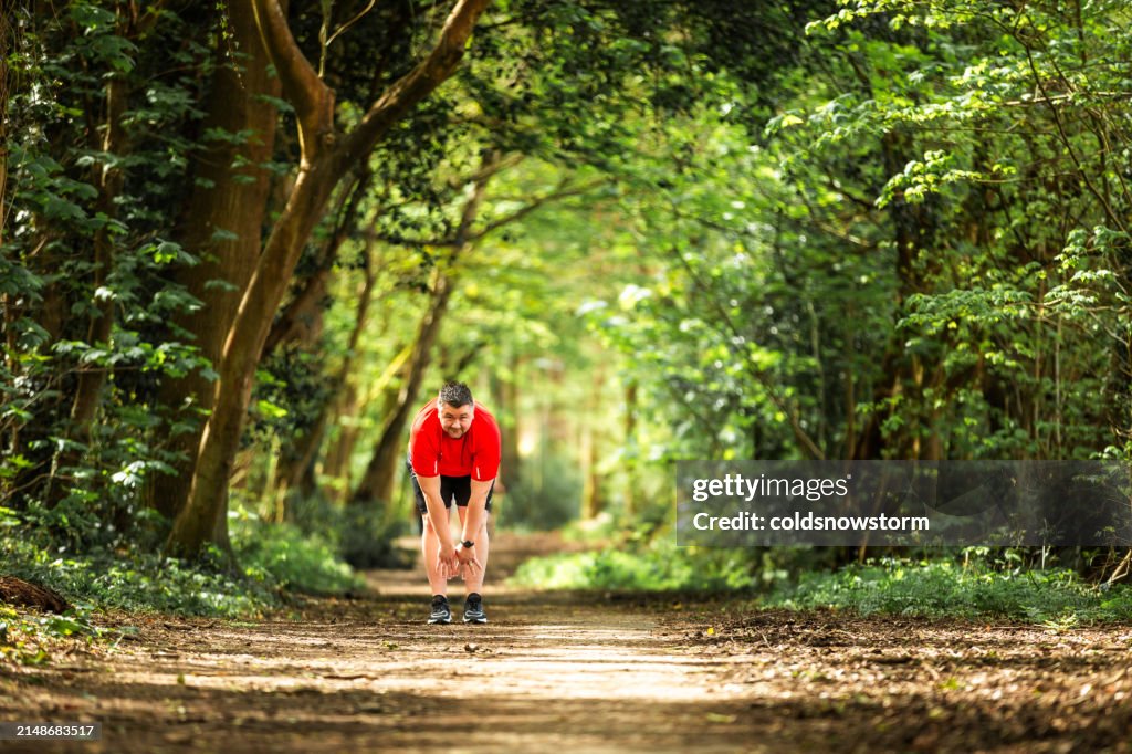 Mid adult man stretching hamstring muscles before running in forest