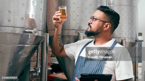 a skilled brewmaster assesses the color and clarity of craft beer, sampling from a stainless-steel brewery tank. professional, dedication, and expert brewing process depicted in an authentic brewery environment. - brouwerij stockfoto's en -beelden
