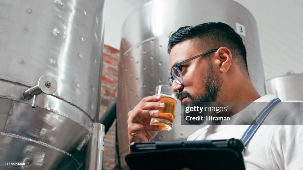 Meticulous brewer in a modern brewery examines the quality of craft beer, carefully analyzing its color and clarity. The stainless steel brewing equipment in the background reinforces the professional environment, symbolizing the detailed art of brewing