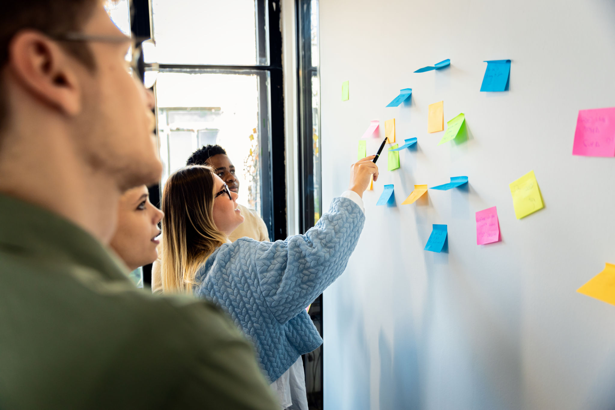 Diverse group of young business people working in office using colorful sticky notes on wall to organize their ideas. Diverse group of young business people working in office using colorful sticky notes on wall to organize their ideas.