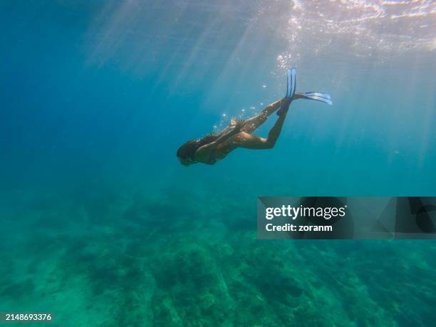 schöne frau in bikini und flossen, die in richtung meeresboden taucht, aufgenommen mit unterwasserkamera - flosse stock-fotos und bilder