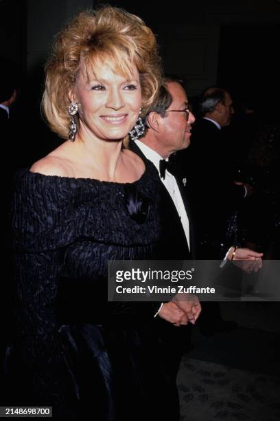 American actress Angie Dickinson, wearing a black off-shoulder outfit, and American film producer Allan Carr, who wears a tuxedo and bow tie, attend...