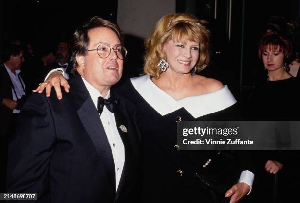 American film producer Allan Carr, wearing a tuxedo and bow tie, and American actress Angie Dickinson, who wears a black-and-white off-shoulder...