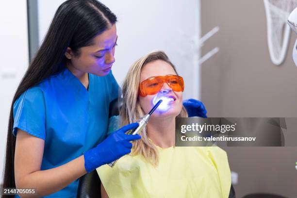 il dentista asiatico fa una procedura di sbiancamento dei denti in clinica a una giovane bella donna. un sorriso sano - sbiancamento dentale foto e immagini stock