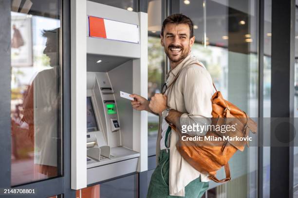 a handsome young man, a tourist, uses an atm to withdraw money - milan markovic stock pictures, royalty-free photos & images