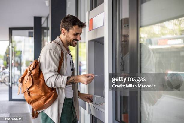 a handsome young man, a tourist, uses an atm to withdraw money - milan markovic stock pictures, royalty-free photos & images