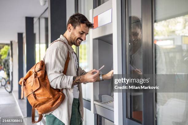 a handsome young man, a tourist, uses an atm to withdraw money - milan markovic stock pictures, royalty-free photos & images