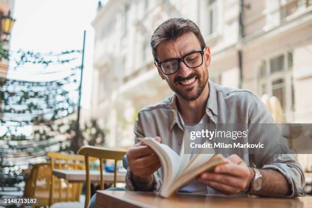 a young man is reading a book while sitting in the garden of a cafe - milan markovic stock pictures, royalty-free photos & images