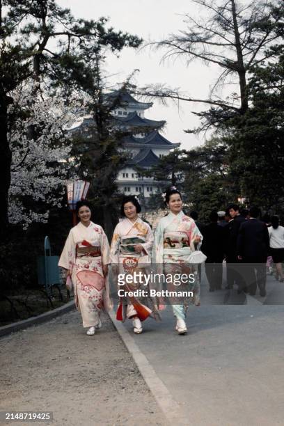 Three Japanese women wearing colourful kimonos walk in the garden of Nagoya Castle, Nagoya, Japan, April 8th 1968. Nagoya Castle can be seen in the...