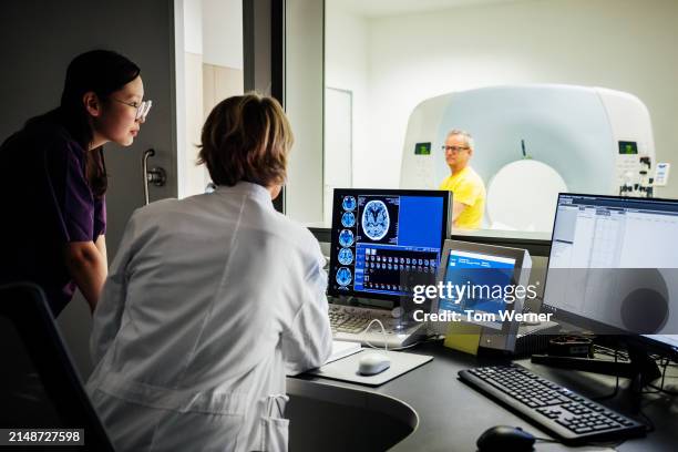 female doctor and nurse looking at patient data of a ct-scan - medizinische forschung stock-fotos und bilder