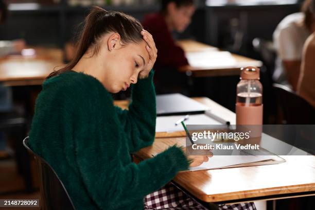 tensed teenage girl writing on paper during exam - examen stockfoto's en -beelden