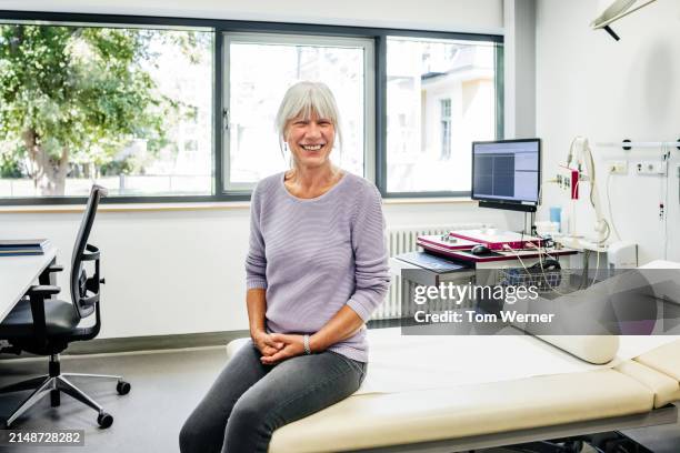 portrait of a senior female patient sitting on examination table - examination table stock pictures, royalty-free photos & images