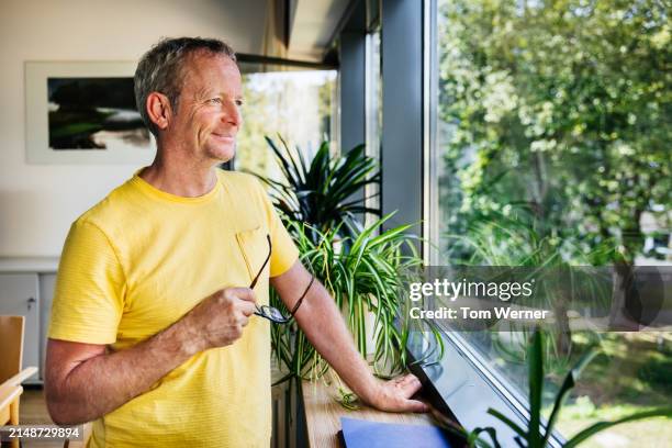 portrait of a senior man enjoying a serene view indoors - guardare fuori dalla finestra foto e immagini stock