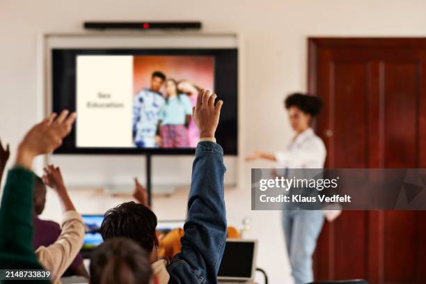 students raising hands with teacher standing by screen - vie scolaire photos et images de collection