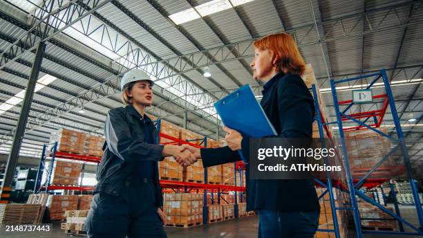 two logistics experts shake hands in agreement inside a warehouse, signifying a successful negotiation or partnership. - strategy execution stock pictures, royalty-free photos & images