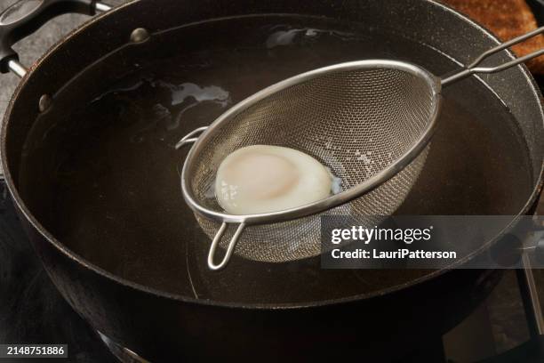 preparing the viral egg poached in a strainer - vergiet stockfoto's en -beelden