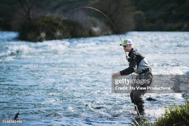 active man catches a fish from the bank of a river - casting stock pictures, royalty-free photos & images