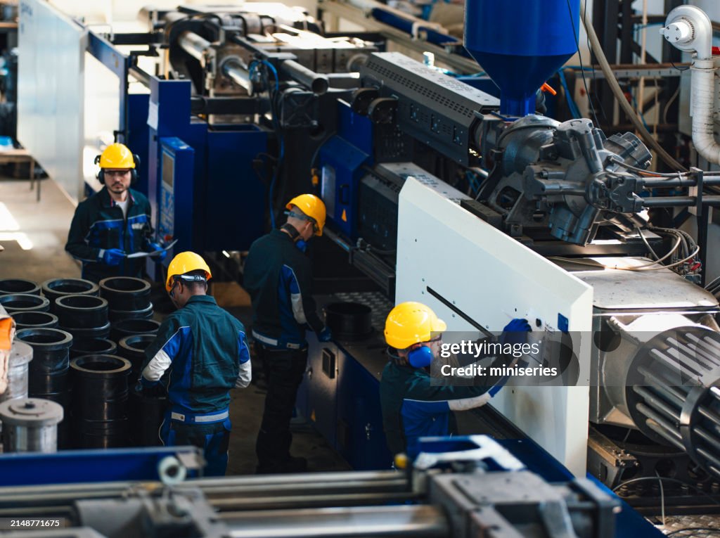 Eine Gruppe von Arbeitern in Sicherheitsausrüstung ist zu sehen, wie sie schwere Maschinen in einer geschäftigen Industriefabrik bedienen und beaufsichtigen, wobei Teamwork und Sicherheit im Vordergrund stehen.