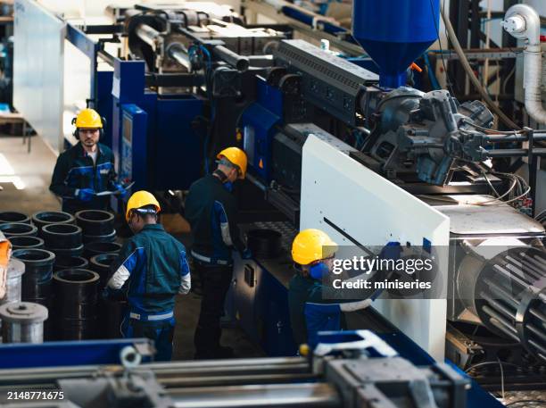 on voit un groupe de travailleurs en tenue de sécurité faire fonctionner et superviser de la machinerie lourde dans une usine industrielle animée, mettant l’accent sur le travail d’équipe et la sécurité. - outil de production photos et images de collection