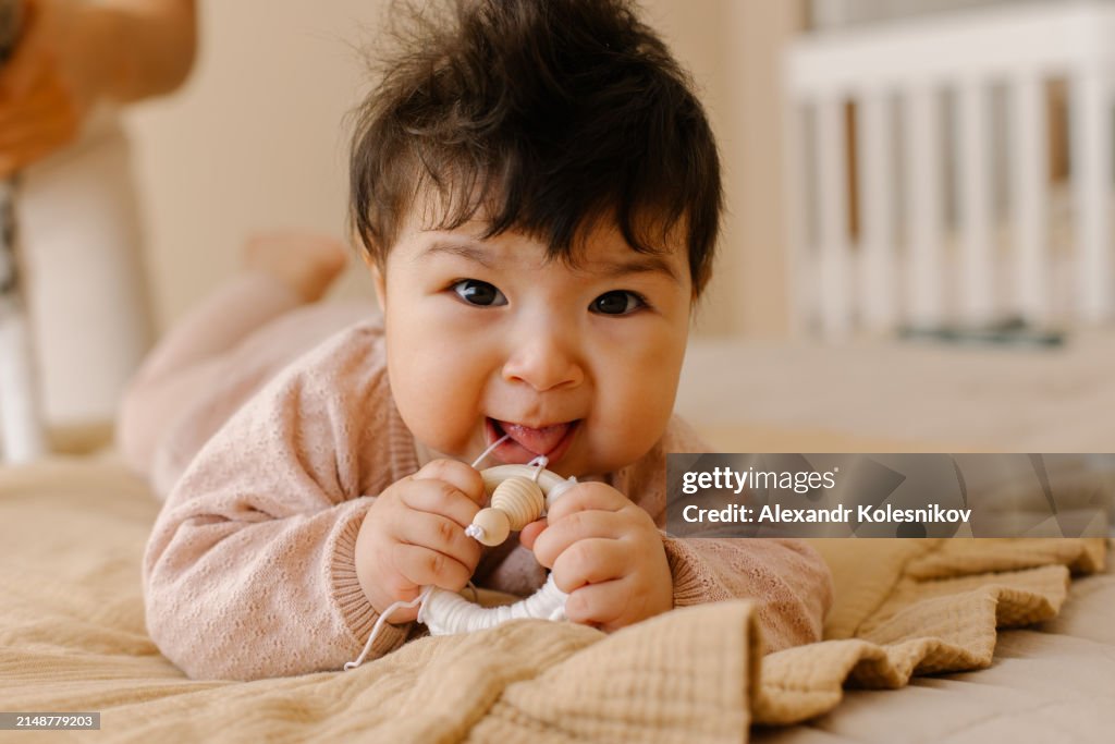 Little baby girl playing with a eco wooden toy on bed at home. Baby development and teething concept
