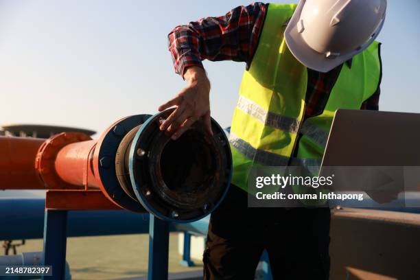 maschinenbauingenieur mit grüner warnweste, schutzhelm, laptop, der an der rohrleitungsleitung arbeitet, industrielle rohrleitungsinstallation - abwasser stock-fotos und bilder