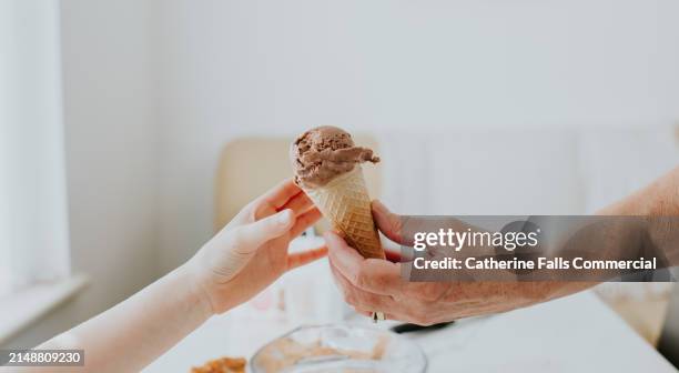simple image of an older adult handing an ice-cream cone containing chocolate ice-cream to a child - passer de main en main photos et images de collection