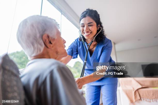 home caregiver examining a senior man at home - female nurse stock pictures, royalty-free photos & images