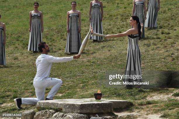Stephanos Ntouskos, First Greek torchbearer receives the flame from Greek actress, Mary Mina, playing the role of the High Priestess, during the...