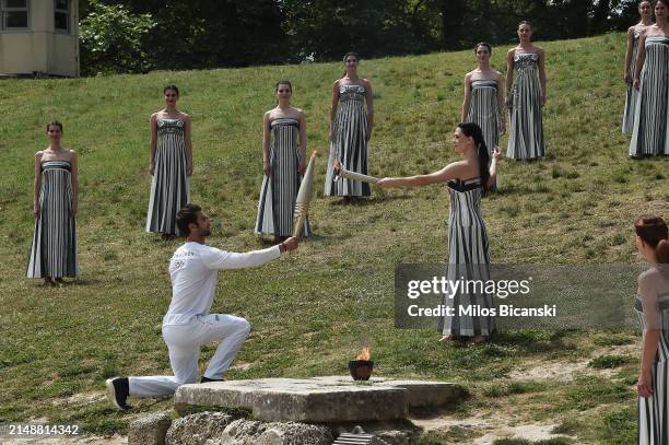 Stephanos Ntouskos, First Greek torchbearer receives the flame from Greek actress, Mary Mina, playing the role of the High Priestess, during the...