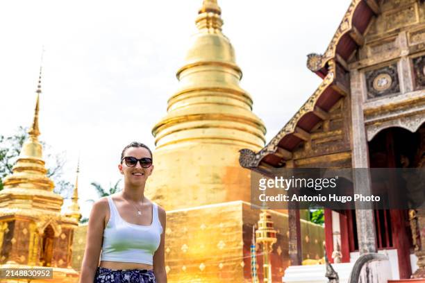young woman posing next to the pagoda at wat phra singh temple in chang mai. - singh stock pictures, royalty-free photos & images