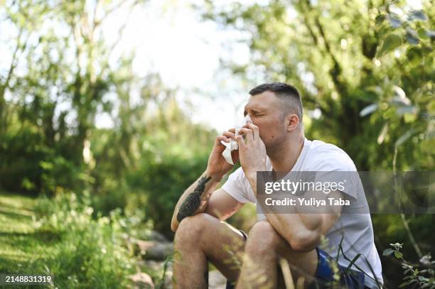 man sneezing in parkland. - cold virus stock pictures, royalty-free photos & images